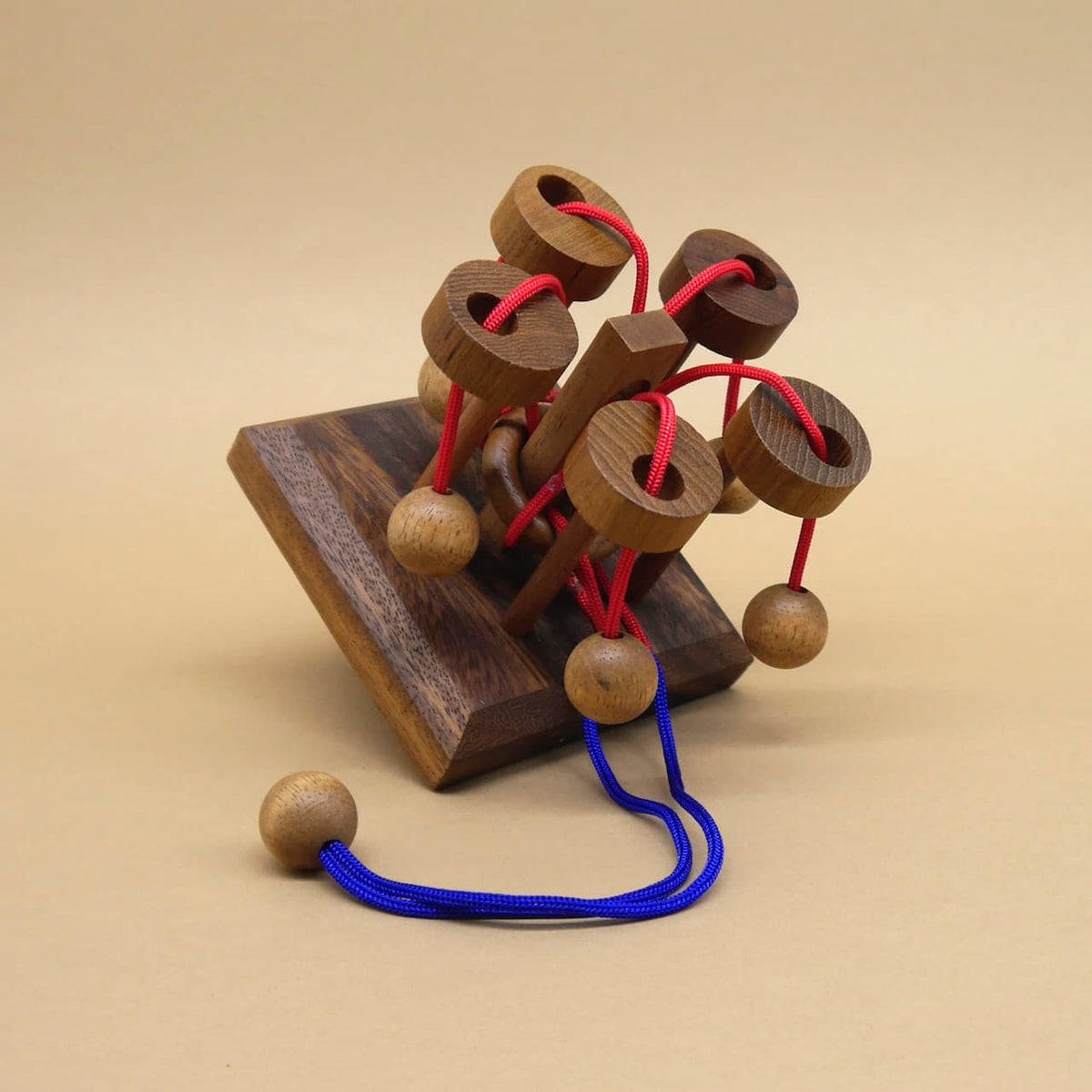 Holzpuzzle mit roten Schnüren, das als kniffliges Karusselpuzzle-Knobelspiel dient.