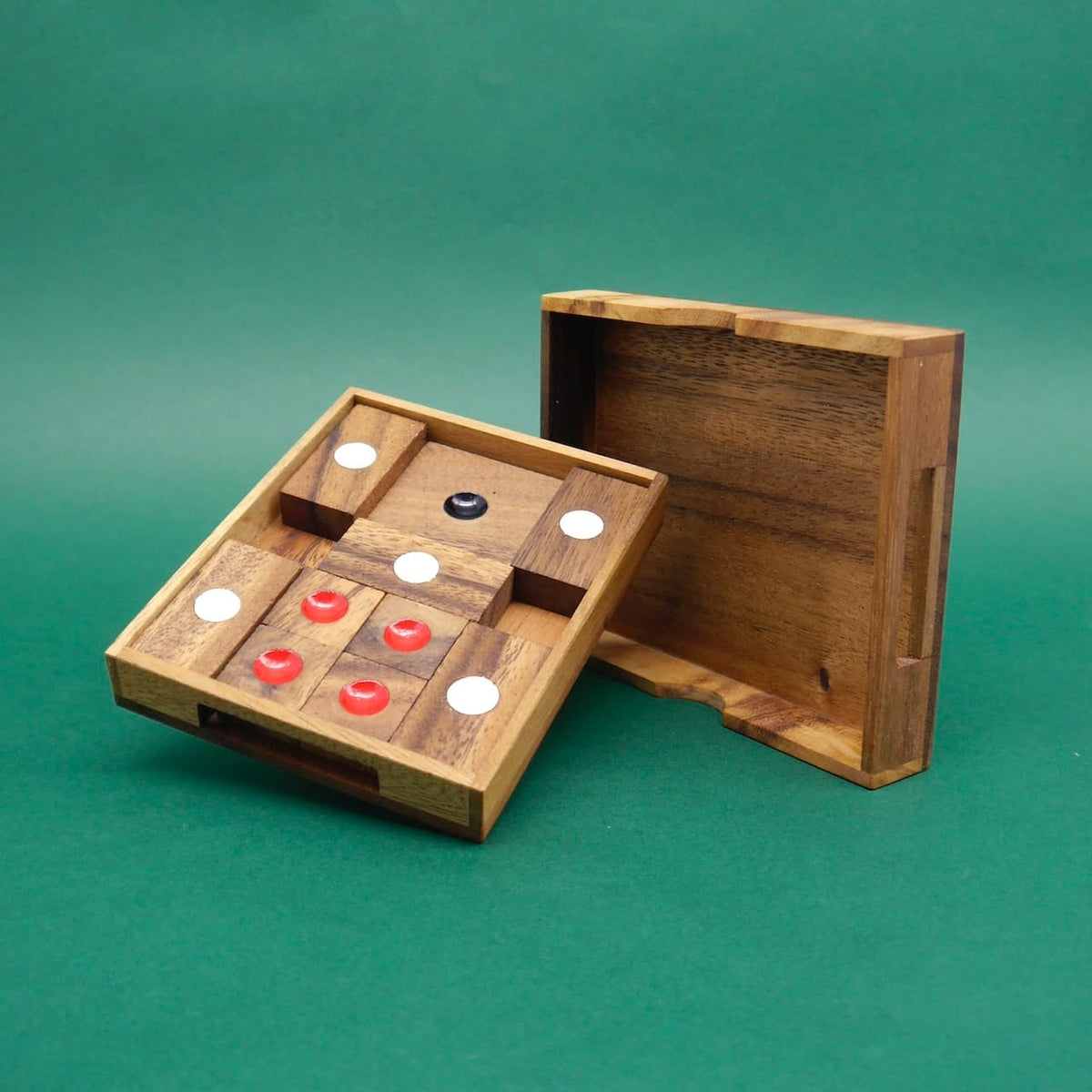 Teilweise bestücktes Holz‑Knobelspiel in einer handlichen Reisebox; Deckel angelehnt, Spielsteine mit Punkten in Schwarz, Weiß und Rot sichtbar.