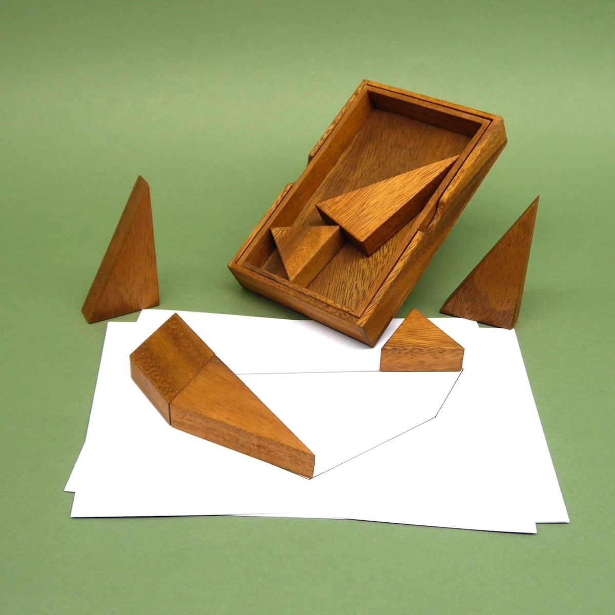 Holz-Tangram als Geduldsspiel für Kinder mit geometrischen Formen auf weißem Papier vor grünem Hintergrund.