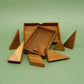 Auseinandergelegtes Holzpuzzle als Knobelspiel mit verschiedenen geometrischen Bausteinen auf grünem Untergrund.