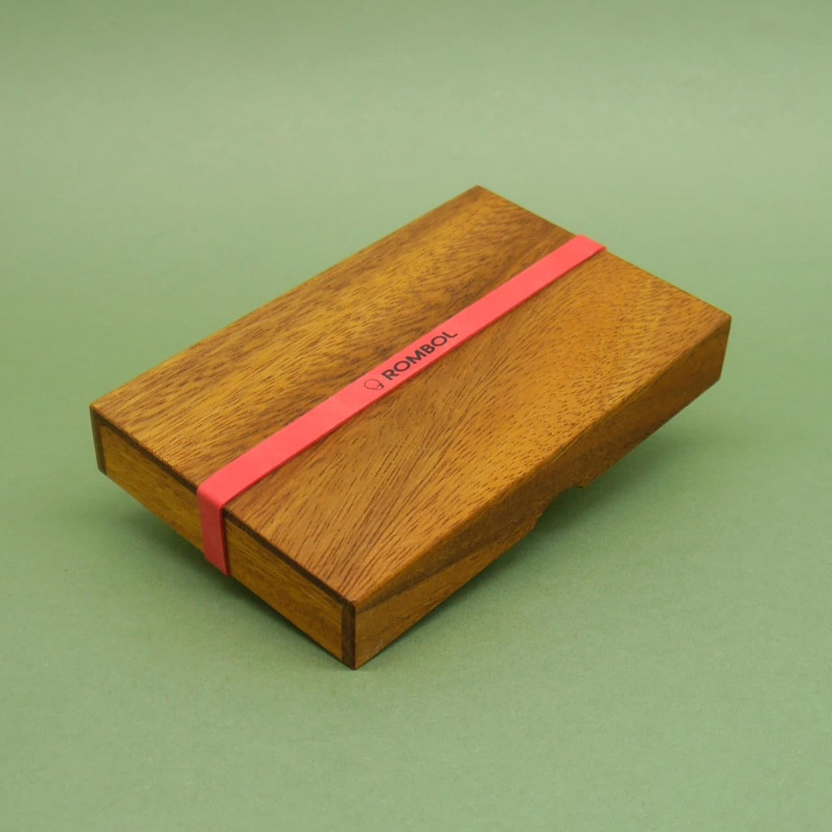 Verschlossenes Logikspiel aus Holz mit rotem Band und der Aufschrift ROMBOL auf grünem Hintergrund.