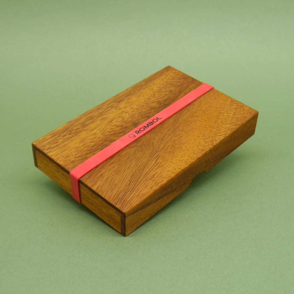 Verschlossenes Logikspiel aus Holz mit rotem Band und der Aufschrift ROMBOL auf grünem Hintergrund.