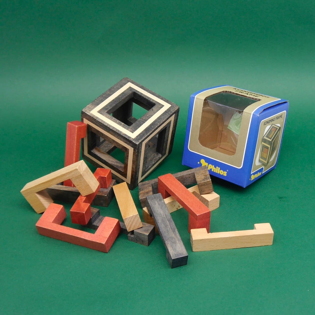Zerlegtes Holzspiel mit bunten Puzzleteilen neben einem fertigen Kongming-Rahmen auf grünem Hintergrund.
