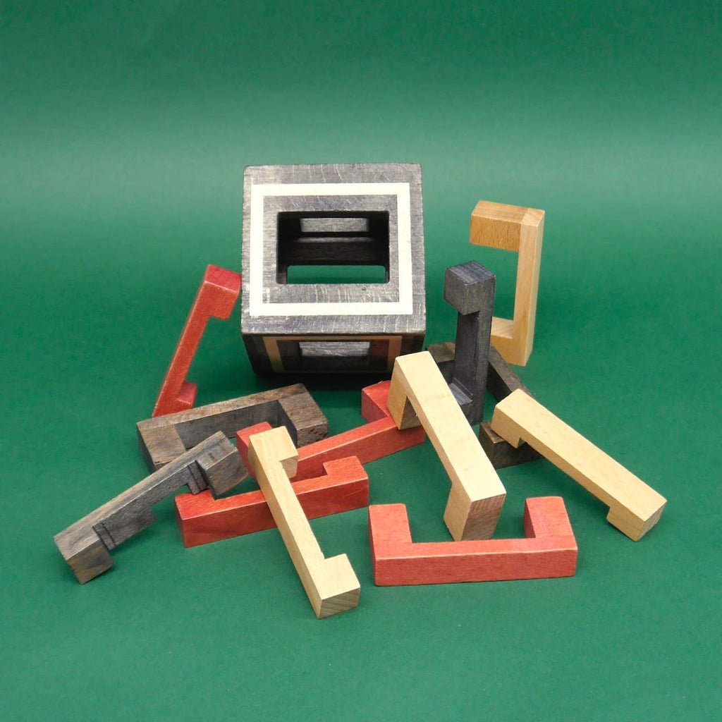 Einzelteile eines Holzpuzzles vor einem teilweise zusammengesetzten Kongming-Würfel aus Holz in verschiedenen Farben.