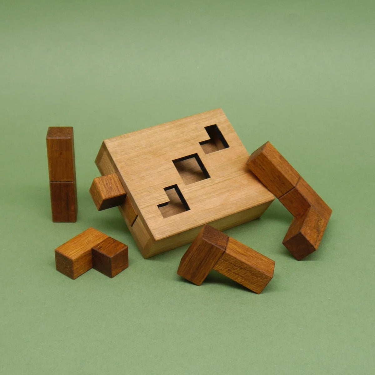 Geduldsspiel: zerlegte winklige Klötzchen liegen um einen quaderförmigen Holzkasten mit Aussparungen.