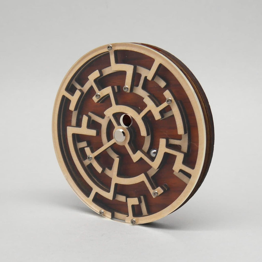 Rundes 3D-Holzpuzzle mit einem komplexen Labyrinthmuster und kleinen Stahlkugeln, stehend aufrecht auf einer hellgrauen Fläche.