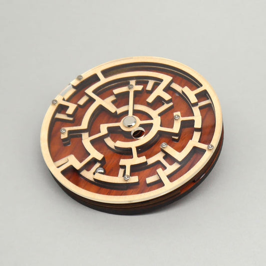 Flach liegendes, rundes Labyrinthspiel aus Holz mit metallischen Kugeln, das zum Knobeln und Nachdenken anregt.