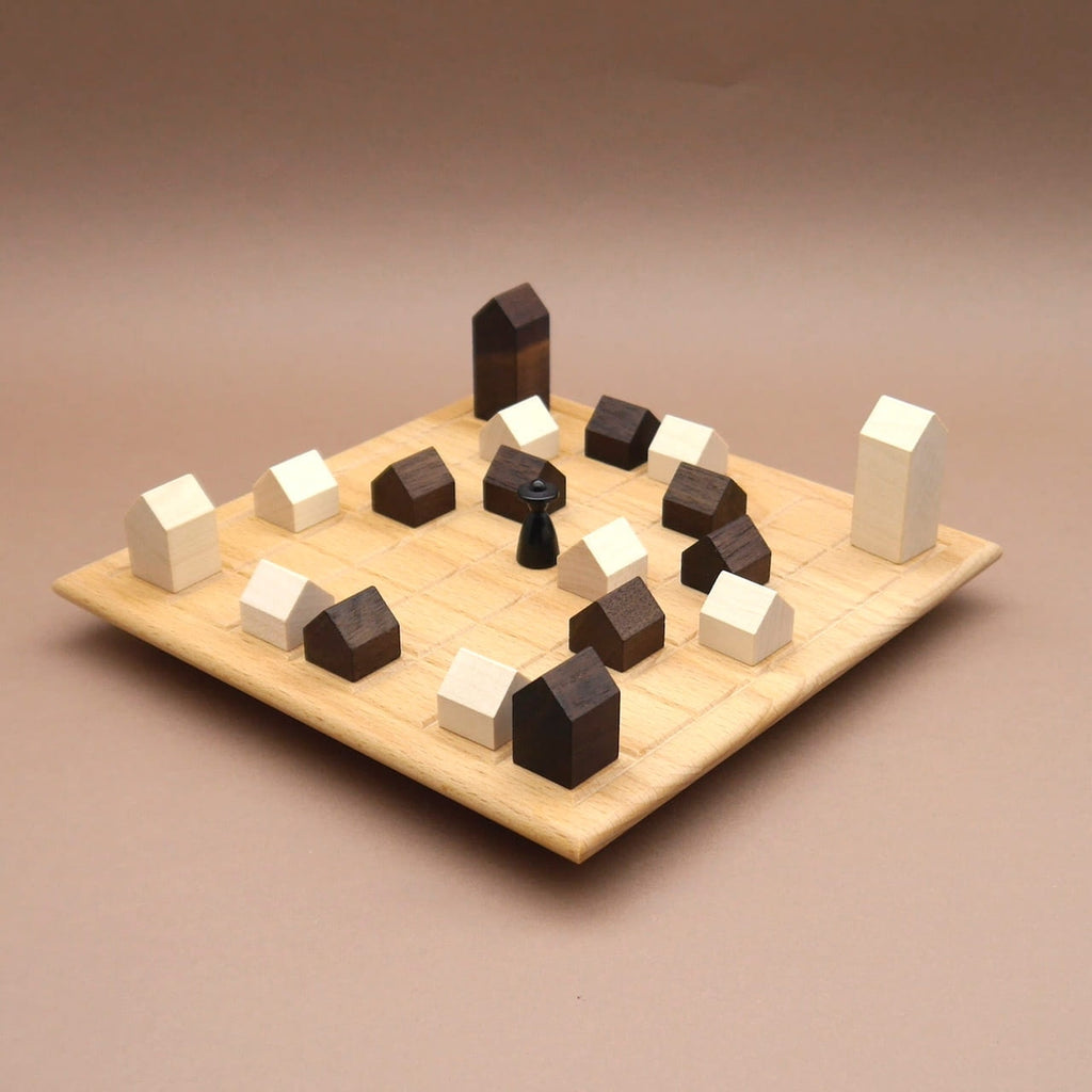 Holz-Brettspiel ‚Lass die Kirche im Dorf‘ mit hellen und dunklen Haus-Steinen und schwarzer Spielfigur auf quadratischem Spielfeld.