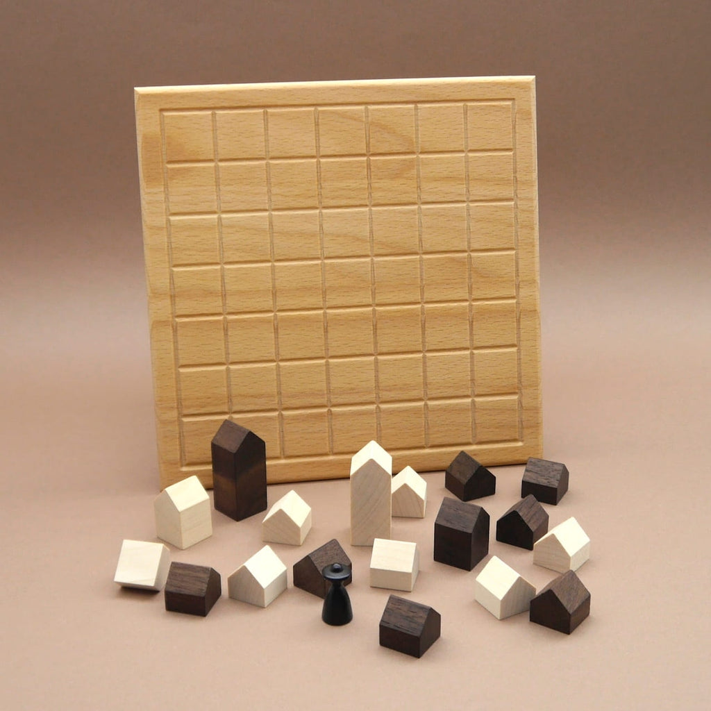 Aufgestelltes Spielfeld mit eingeprägtem Raster; Holz-Häuser liegen davor – das Familienspiel ‚Lass die Kirche im Dorf‘ vor neutralem Hintergrund.