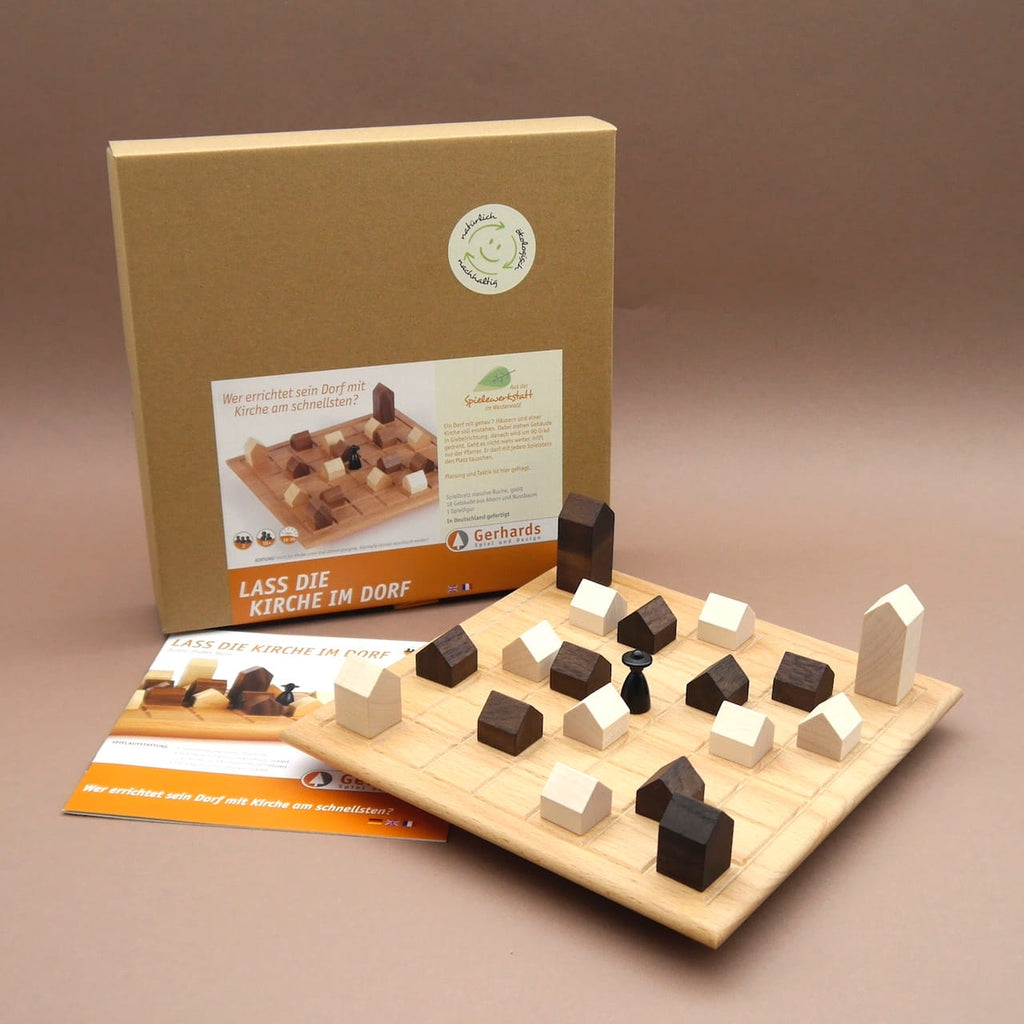 Holzspiel ‚Lass die Kirche im Dorf‘ komplett: bestücktes Spielbrett mit Häusern, schwarze Figur, Anleitung und Karton im Hintergrund.