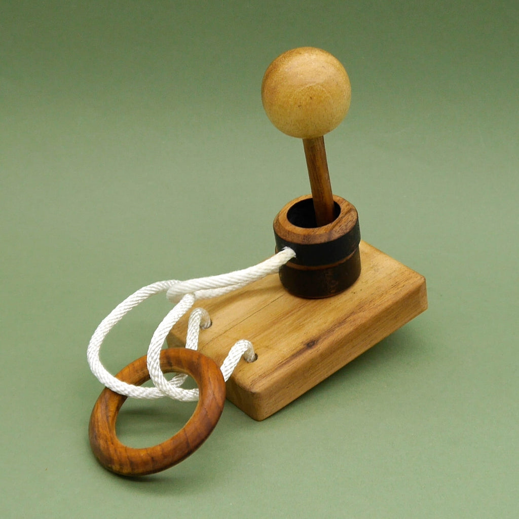 Laterne Seilpuzzle: Holzkugel auf Stab über dunklem Ring, weißes Seil verbindet Sockel mit hölzernem Ring.