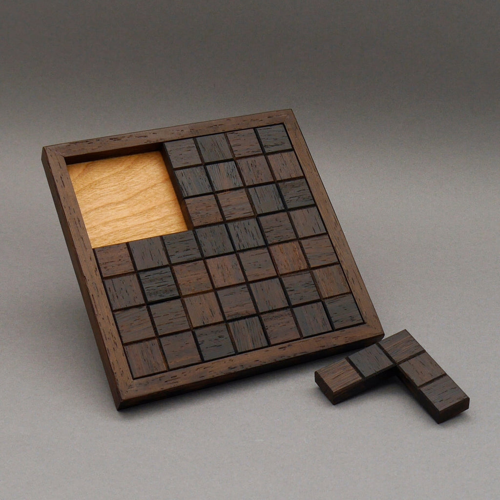 Fast vollständig gelegtes Knobelspiel aus dunklen Holzquadraten in einem Rahmen, ein Puzzleteil fehlt noch.