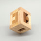 Geschlossener Holzwürfel aus hellem und dunklem Holz lädt zum Knobeln ein; sein geometrisches Innenmuster ist durch die seitlichen Öffnungen sichtbar.