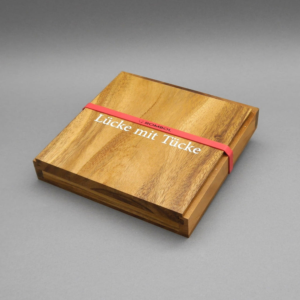 Kompaktes Strategiespiel „Lücke mit Tücke“ in Holzbox, mit rotem Gummiband umspannt; klare, natürliche Holzmaserung.