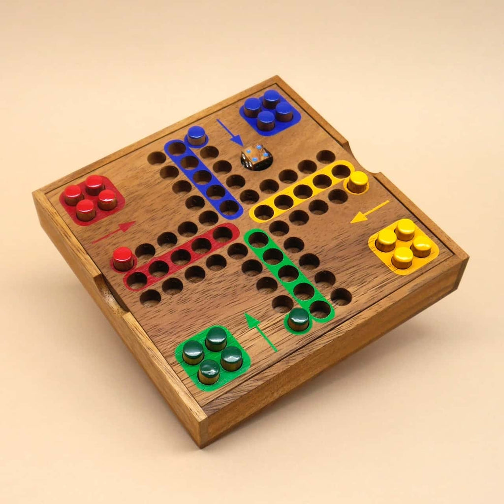 Spielbereites Ludo Würfelspiel aus Holz mit bunten Stecksteinen und eingelassenen Spielfeldern, Perspektive von schräg oben.