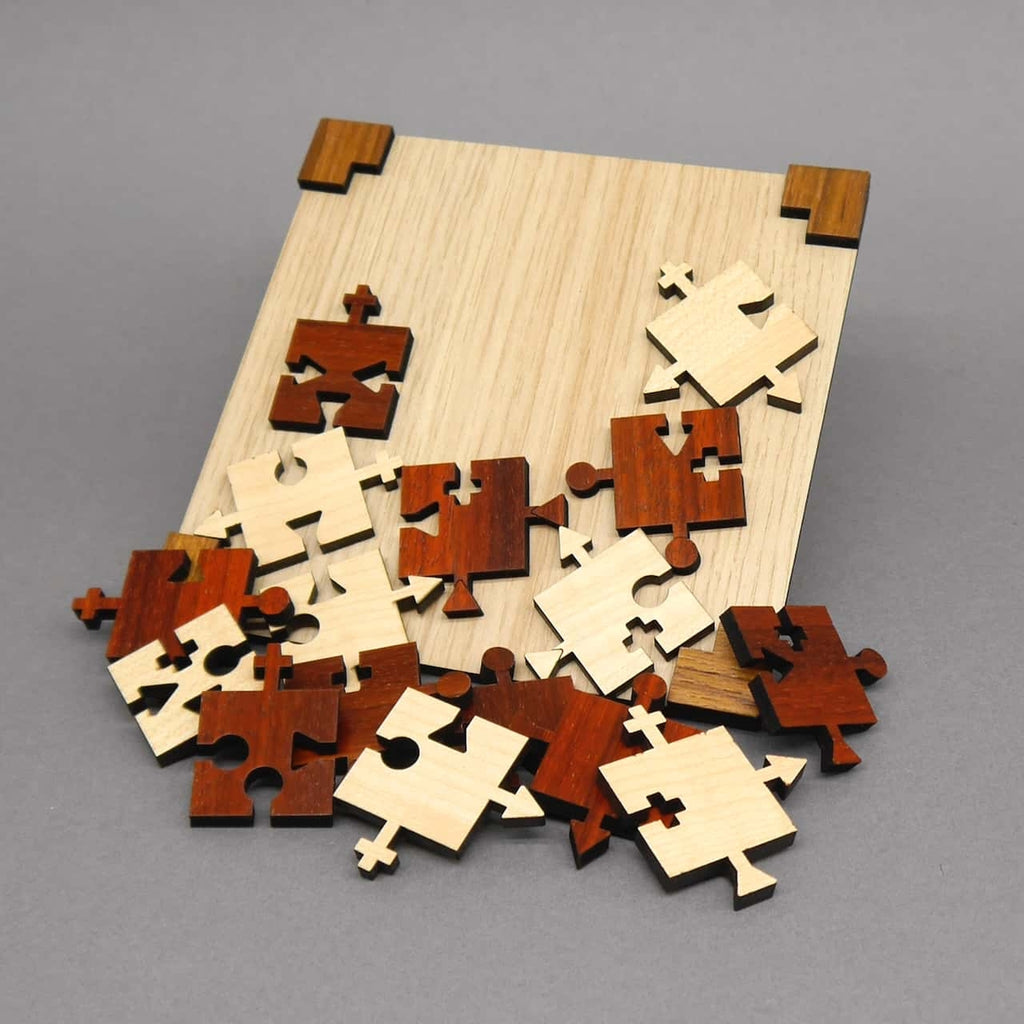 Geneigtes leeres Holzbrett, vor dem rotbraune und helle Puzzleteile mit Pfeil-, Kreis- und Plus-Verbindern verstreut liegen.