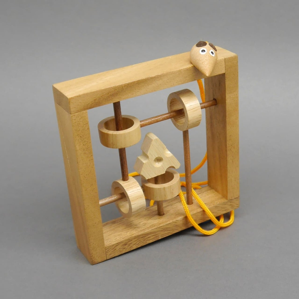 Kompaktes Holz-Knobelspiel: Rahmen mit Stäben, Holzringen, Käseform und orangefarbener Seilschlaufe, Mauskopf lugt oben hervor.