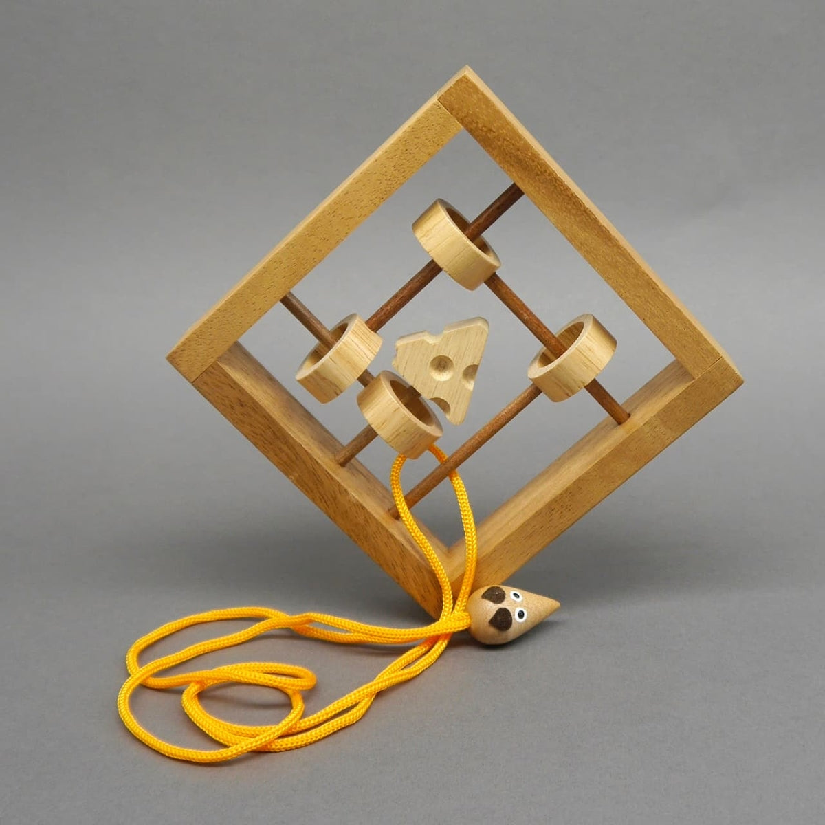 Schräg stehendes Holz-Schnurpuzzle in Mausefalle-Optik; Ringe, Käse und gelbe Schnur mit kleiner Mausfigur bilden das Rätsel.