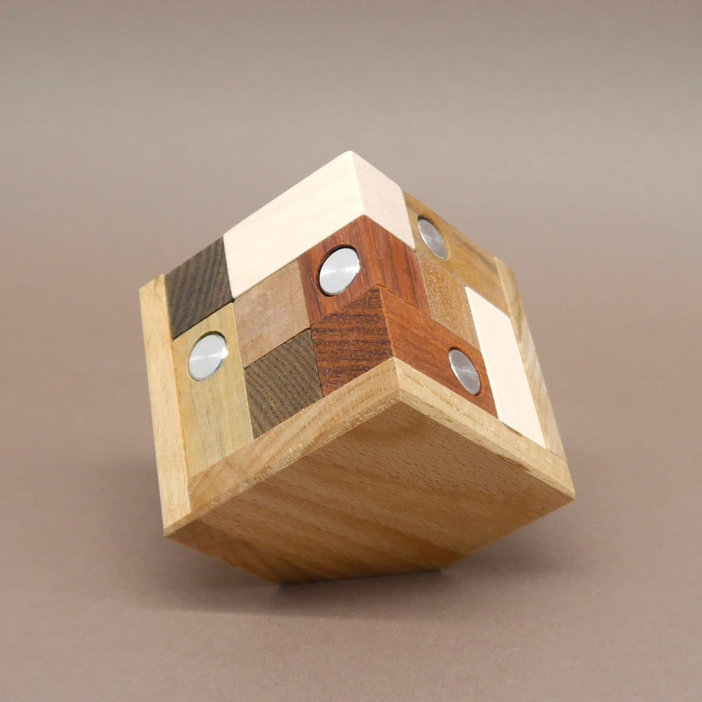 Würfelförmiges Holzpuzzle aus verschiedenfarbigen Holzarten mit integrierten Metallzylindern, zusammengesteckt zu einem massiven Würfel.