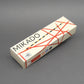 Hellbeige Mikado-Verpackung mit rotem Linienmuster und schwarzem Schriftzug, schräg auf neutral grauem Hintergrund fotografiert.