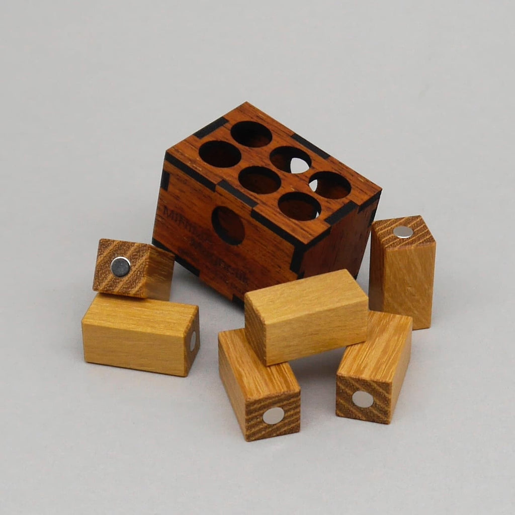 Holzernes Minima Magnetik Denkspiel: eine offene Knobelbox aus dunklem Holz mit mehreren runden Öffnungen und verstreut liegenden helle-Holz-Steinen mit Magnetpunkten.
