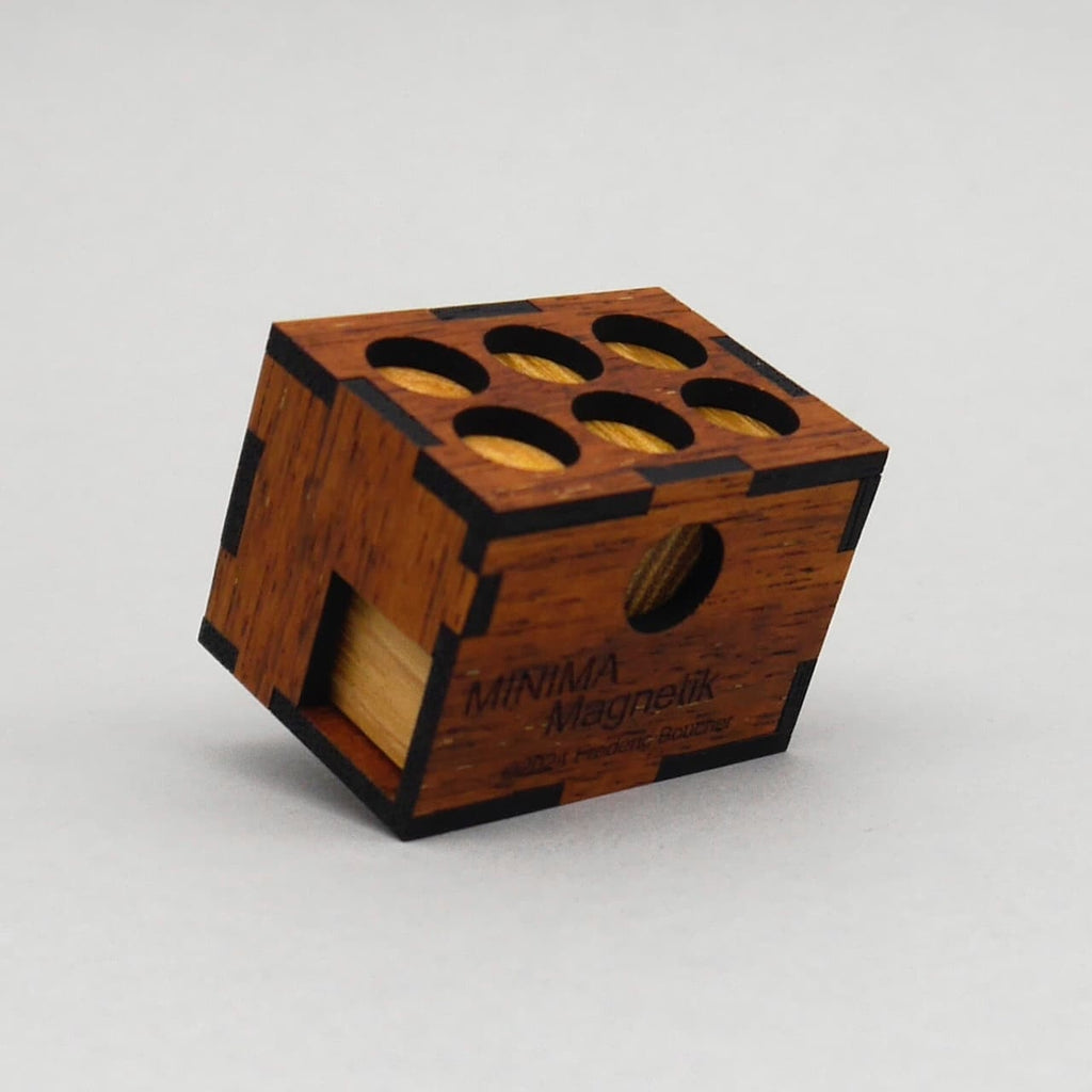 Schräg stehendes Minima Magnetik Holzpuzzle mit sechs runden Aussparungen oben, dunklen Eckverbindungen und sichtbarem Schriftzug auf der Vorderseite.