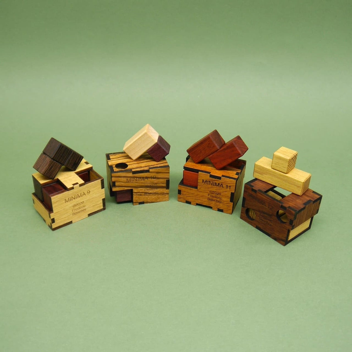 Vier kleine Holzpuzzle-Boxen der Minima-Serie stehen nebeneinander, ihre zerlegten Teile liegen locker darauf – perfekte Knobelspiele vor einem hellgrünen Hintergrund.