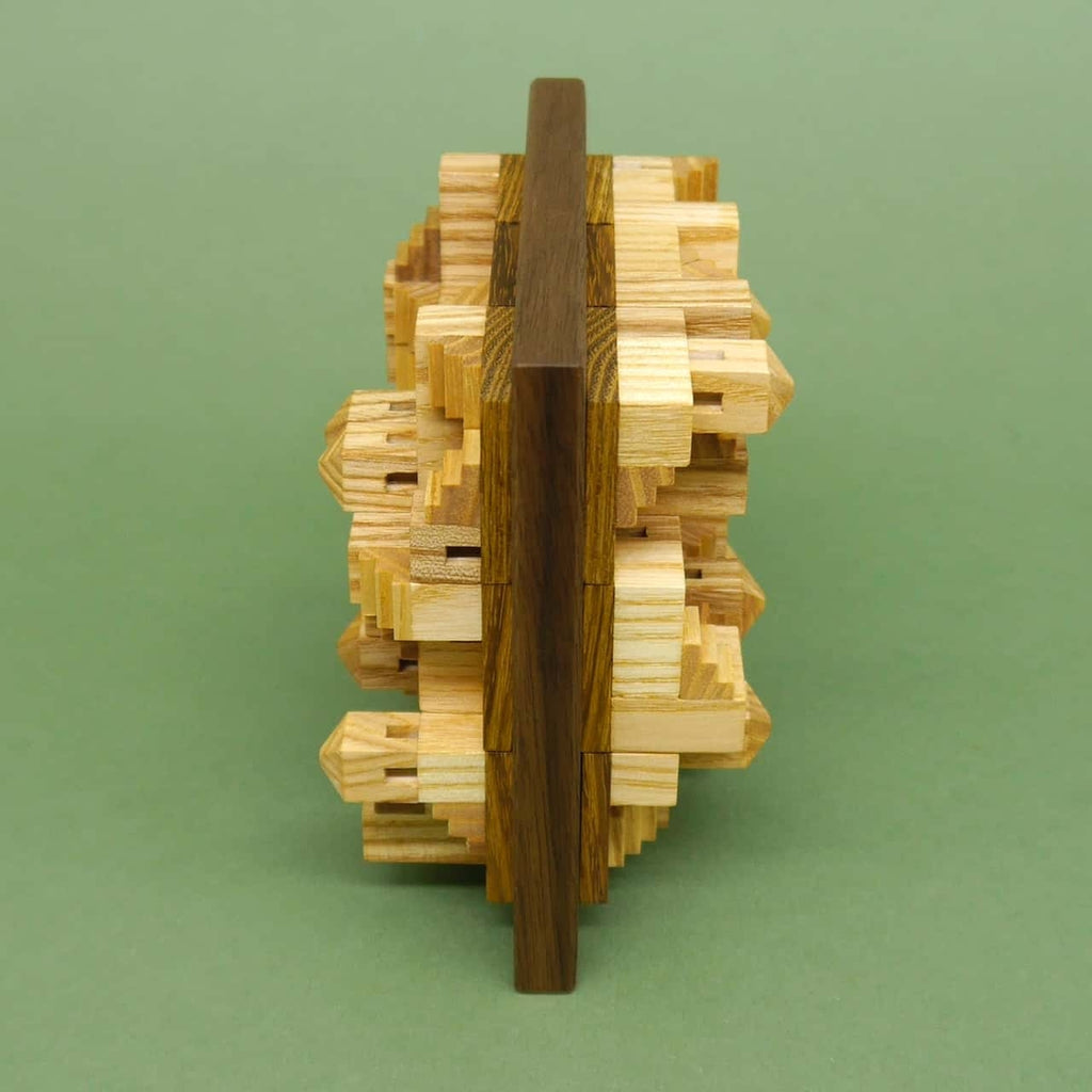 Seitenansicht eines komplexen 3D-Holzpuzzles mit ineinandergreifenden Zähnen aus hellem und dunklem Holz auf grünem Hintergrund.