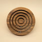 Frontale Ansicht eines runden Holz‑Geduldspiel‑Labyrinths mit konzentrischen Rillen; zwei kleine Stahlkugeln ruhen im unteren Bereich.