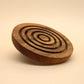 Schräg aufliegendes Holz‑Kinderspiel in Form eines runden Labyrinths aus konzentrischen Ringen, derzeit ohne sichtbare Kugeln.