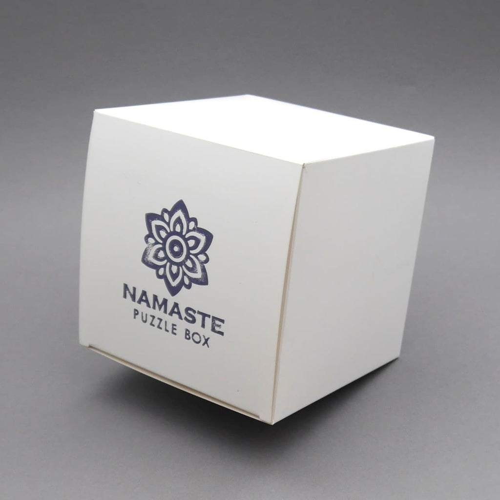 Namaste Puzzle Box – Logikpuzzle in schlichter weißer Verpackung mit Logo, vor grauem Hintergrund.
