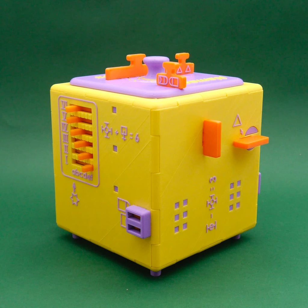 Namaste Knobelwürfel in Gelb/Lila/Orange mit Zahnrad-Unterseite, Schieberiegeln und seitlicher Zahlenskala, studiofotografiert.