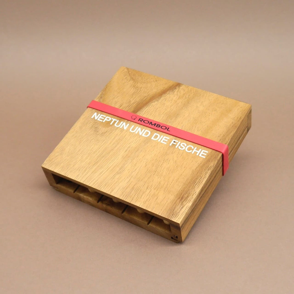 Quadratische Box des Holzspiels „Neptun und die Fische“, sicher verschlossen mit rotem Gummiband, Steckfächer unten erkennbar.
