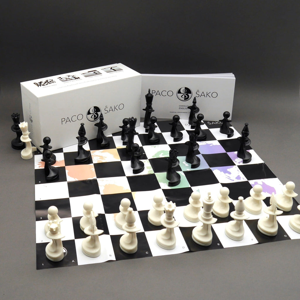 Paco Sako Schachspiel mit aufgebautem Spielbrett, Figuren, Verpackung und Spielanleitung auf grauem Hintergrund.