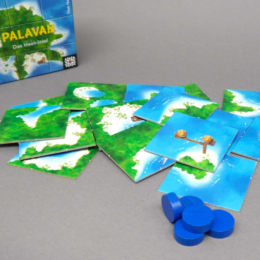 Mehrere quadratische Insel-Kacheln und blaue Holzchips des Familienspiels „Palavan“ liegen locker verstreut auf grauem Untergrund.