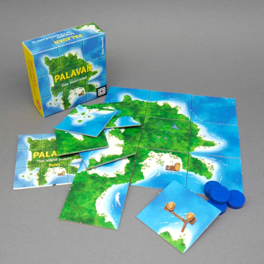 Ausgelegte Kacheln bilden eine zusammenhängende Insel, während weitere Teile, Anleitung und blaue Chips das Legespiel „Palavan“ als rätselhaftes Gesellschaftsspiel zeigen.