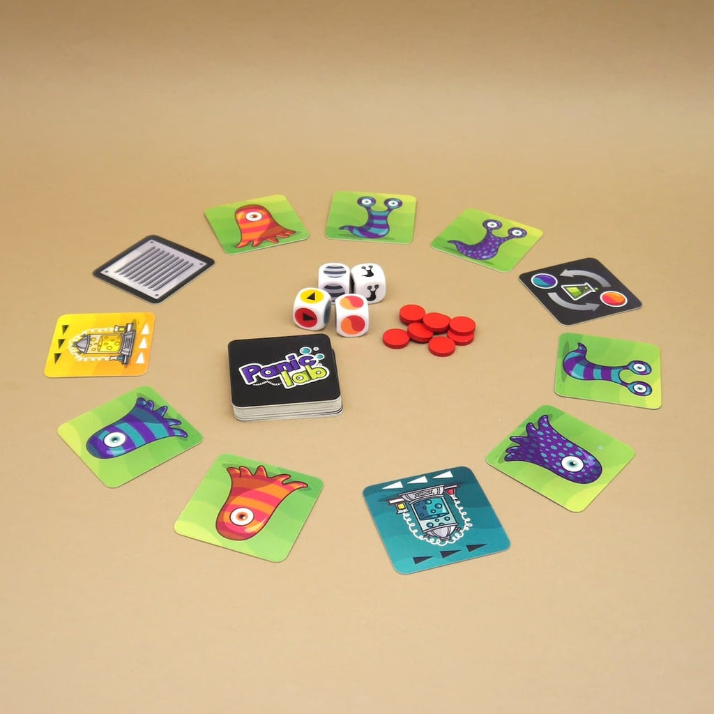 Panic Lab Gesellschaftsspiel mit bunten Monster-Karten, Würfeln und roten Chips kreisförmig auf hellem Tisch.