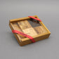 Geschenkverpacktes IQ‑Puzzle in Holzbox mit Klarsichtdeckel und rotem ROMBOL‑Band.