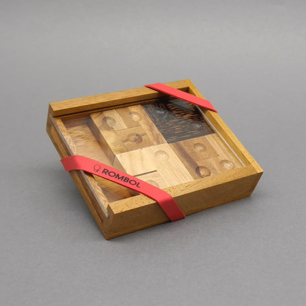 Geschenkverpacktes IQ‑Puzzle in Holzbox mit Klarsichtdeckel und rotem ROMBOL‑Band.