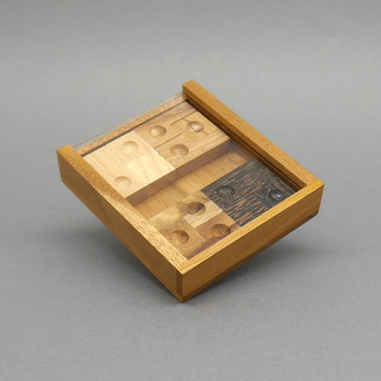 Quadratische Holzbox mit transparentem Deckel zeigt sortierte Spielsteine eines kniffligen Schiebepuzzle.