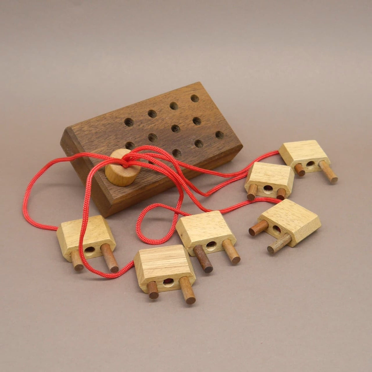 Holzspielzeug mit roten Schnüren und Steckelementen auf einem Holzbrett – ein kreatives 3D Puzzle zum Knobeln und Verschenken.