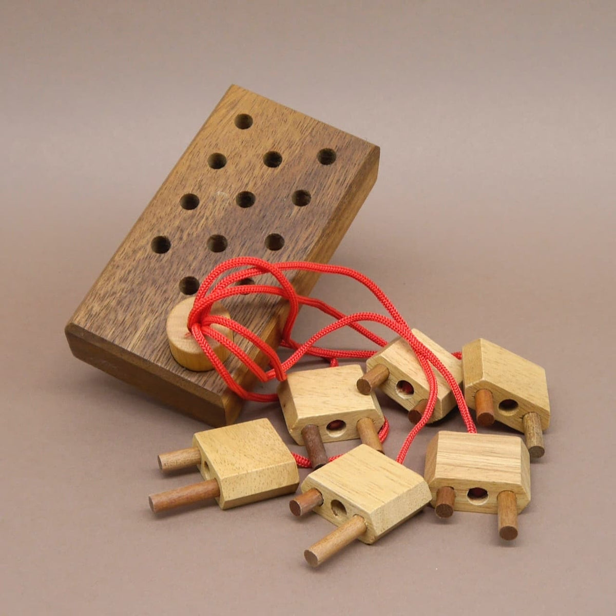 Ein liebevoll gefertigtes Geduldspiel aus Holz mit mehreren Steckerteilen und roten Schnüren, ideal zur Förderung logischen Denkens.