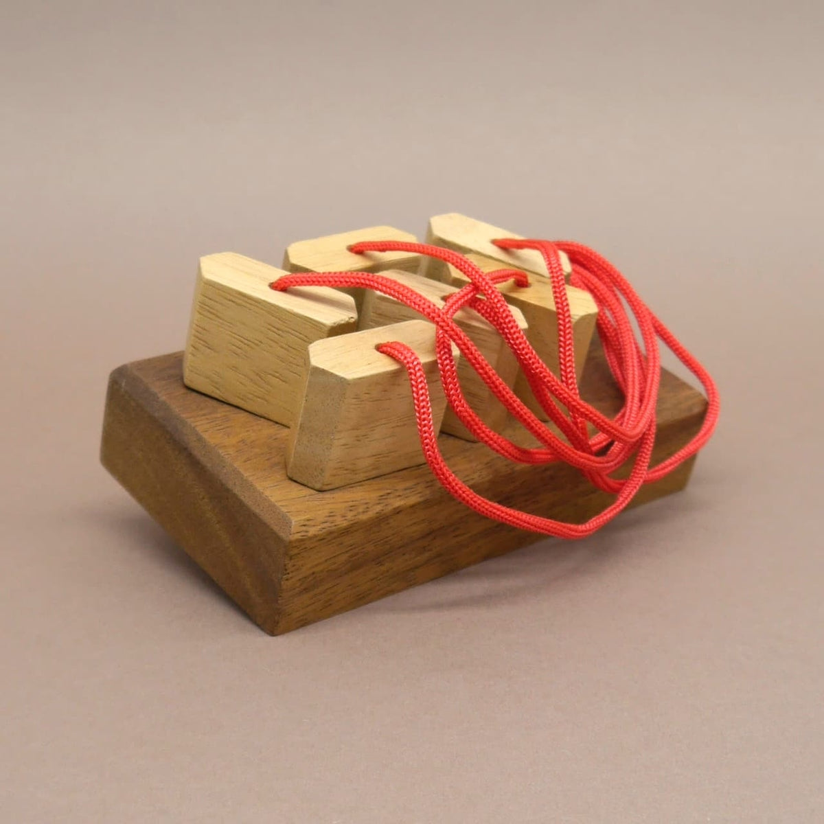 Ein komplexes Knobelspiel aus Holz mit roten Schnüren, bei dem mehrere Stecker in ein Brett eingepasst werden müssen.