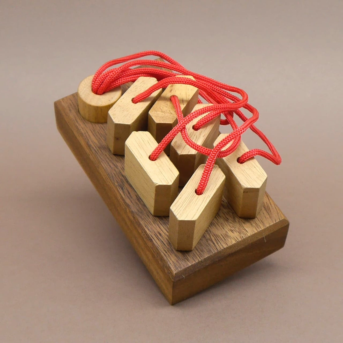 Ein handgefertigtes Steckpuzzle aus Holz mit mehreren Einsätzen und roten Schnüren – ein anspruchsvolles Denkspiel für Jung und Alt.