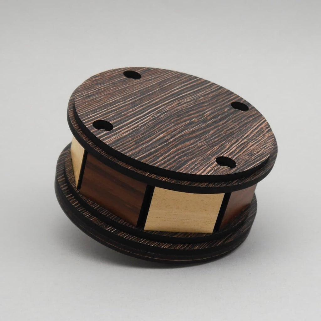 Runde Holz-Geduldspiel-Box mit dunklem Deckel und hellen seitlichen Paneelen.