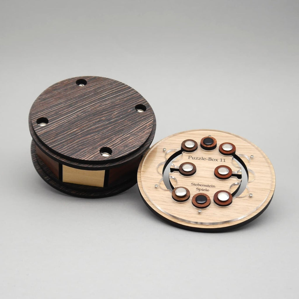 Geöffnete Geschenkbox aus Holz mit sichtbar freigelegtem Puzzle-Mechanismus neben der runden Box.