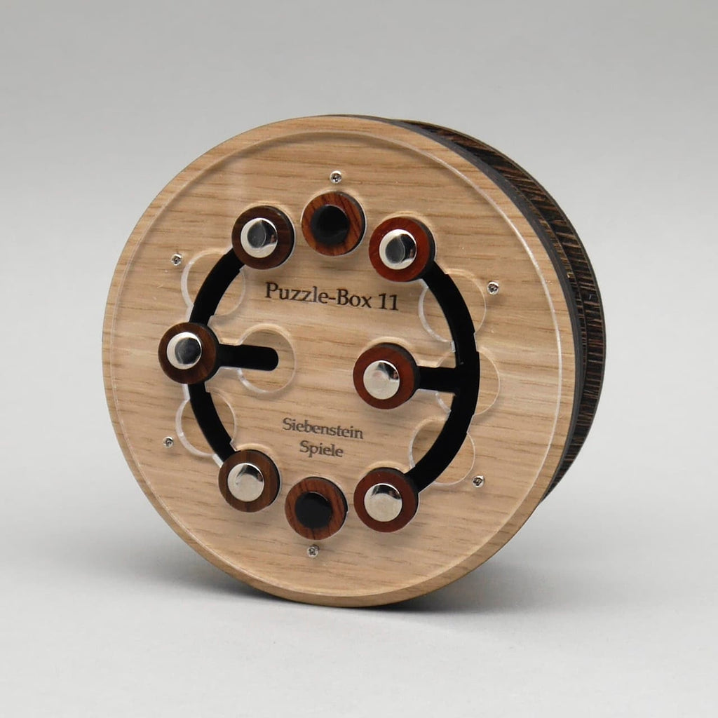 Runde Trickkiste aus hellem Holz mit kreisförmig angeordneten Knöpfen und sichtbarem Denkspiel-Mechanismus.
