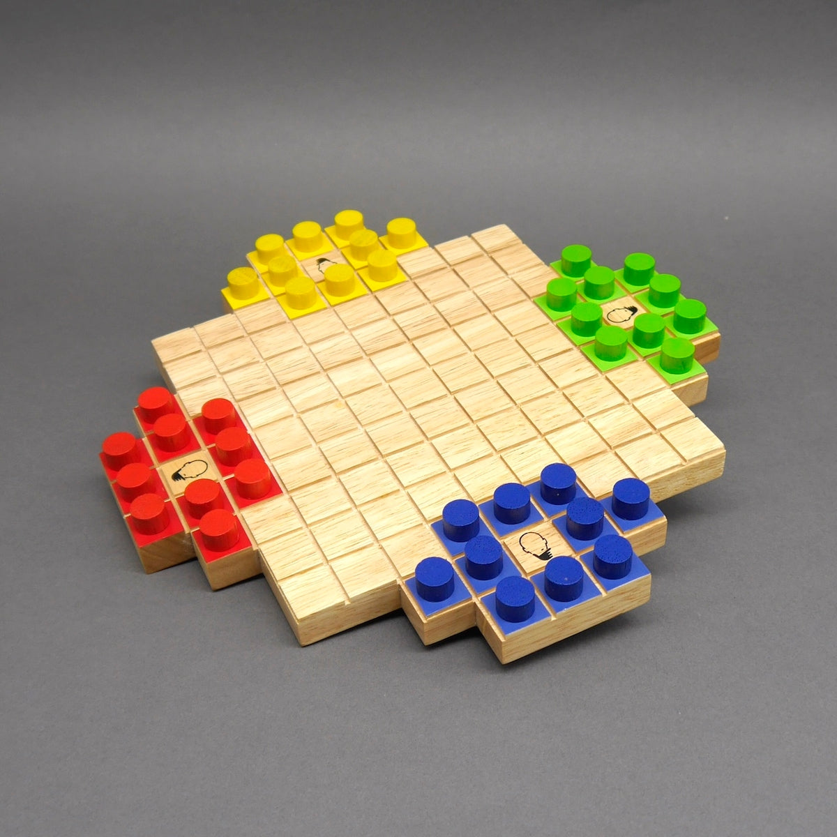 Quadratisches Brettspiel aus hellem Holz mit farbigen Holzfiguren in vier Ecken auf grauem Hintergrund.