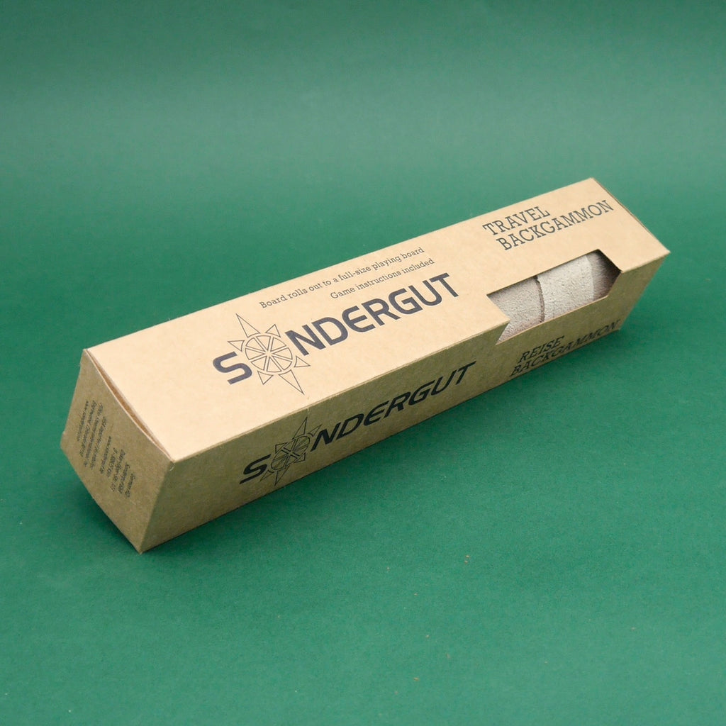 Verpackung des Sondergut Reise-Backgammon Lederspiel – längliche Kartonschachtel auf grünem Hintergrund.