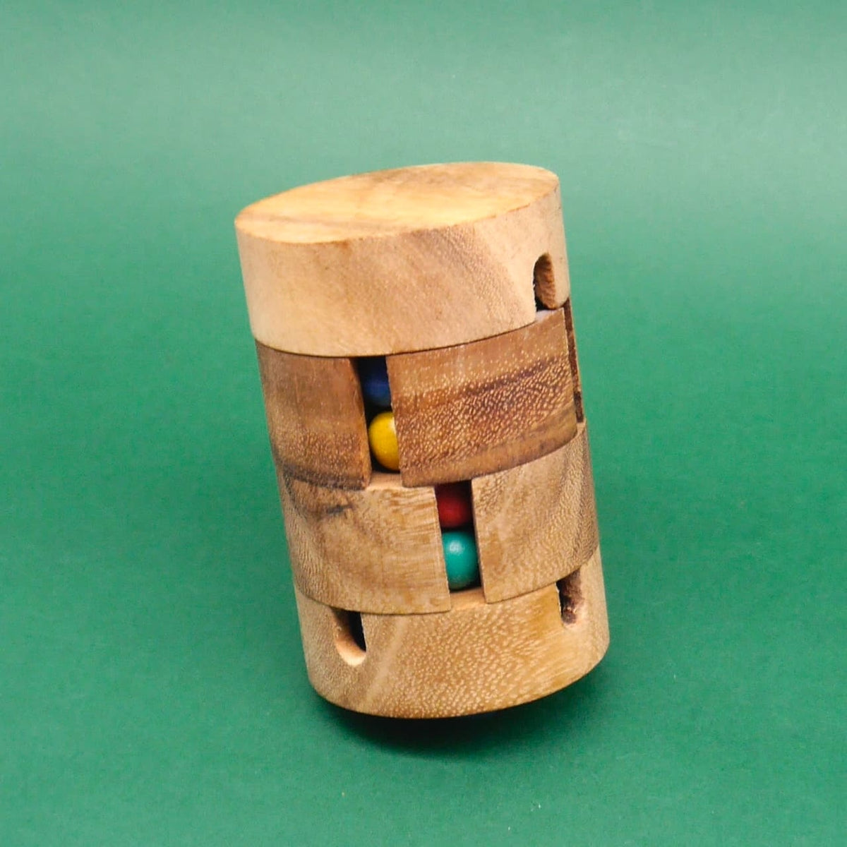 Leicht schräg positioniertes Holzpuzzle in Zylinderform, dessen versetzte Schlitze bunte Kugeln (Gelb, Blau, Rot, Türkis) preisgeben.